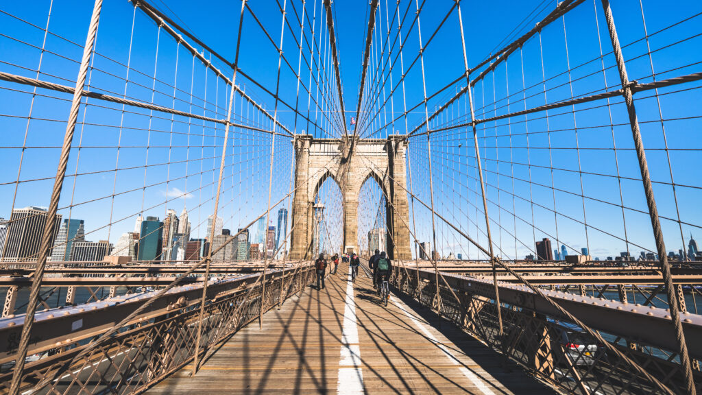 People walking and riding bicycles on Brooklyn bridge in New York City.